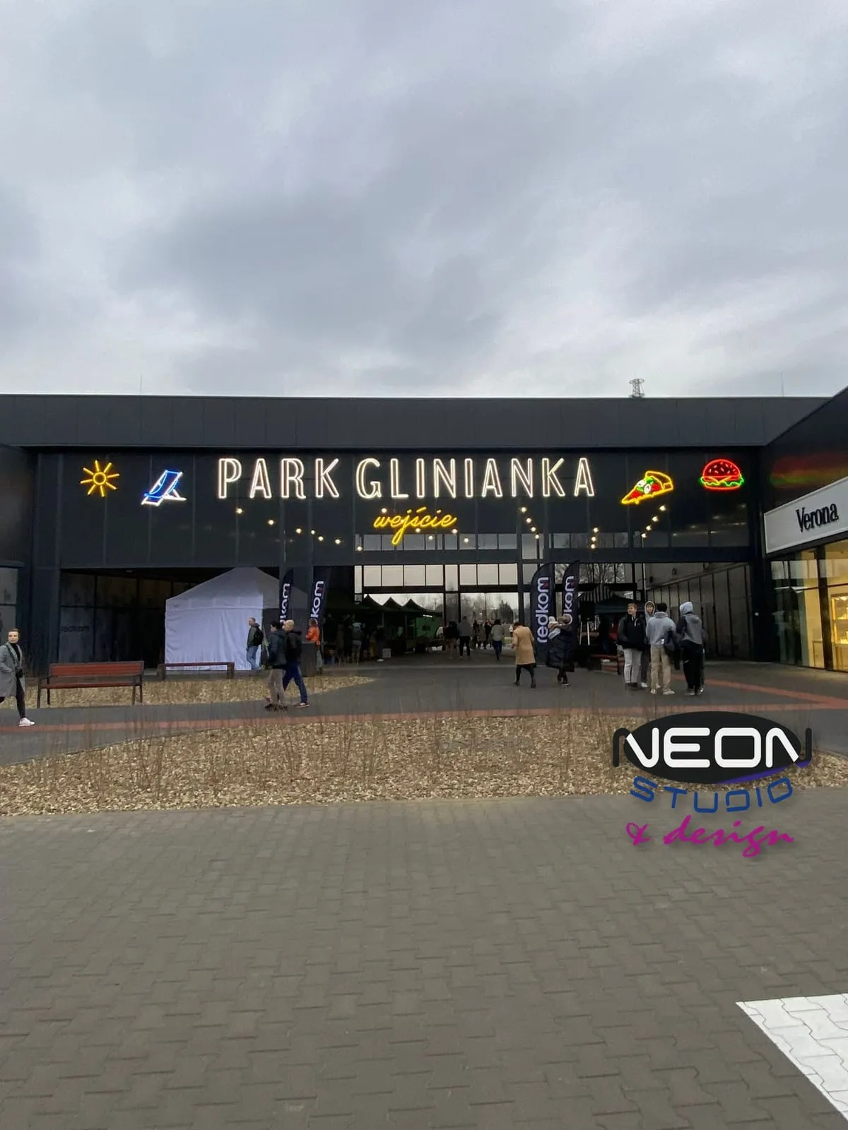 Park Glinianka — white glass neons with the centre’s name and a yellow „entrance” neon on the building facade