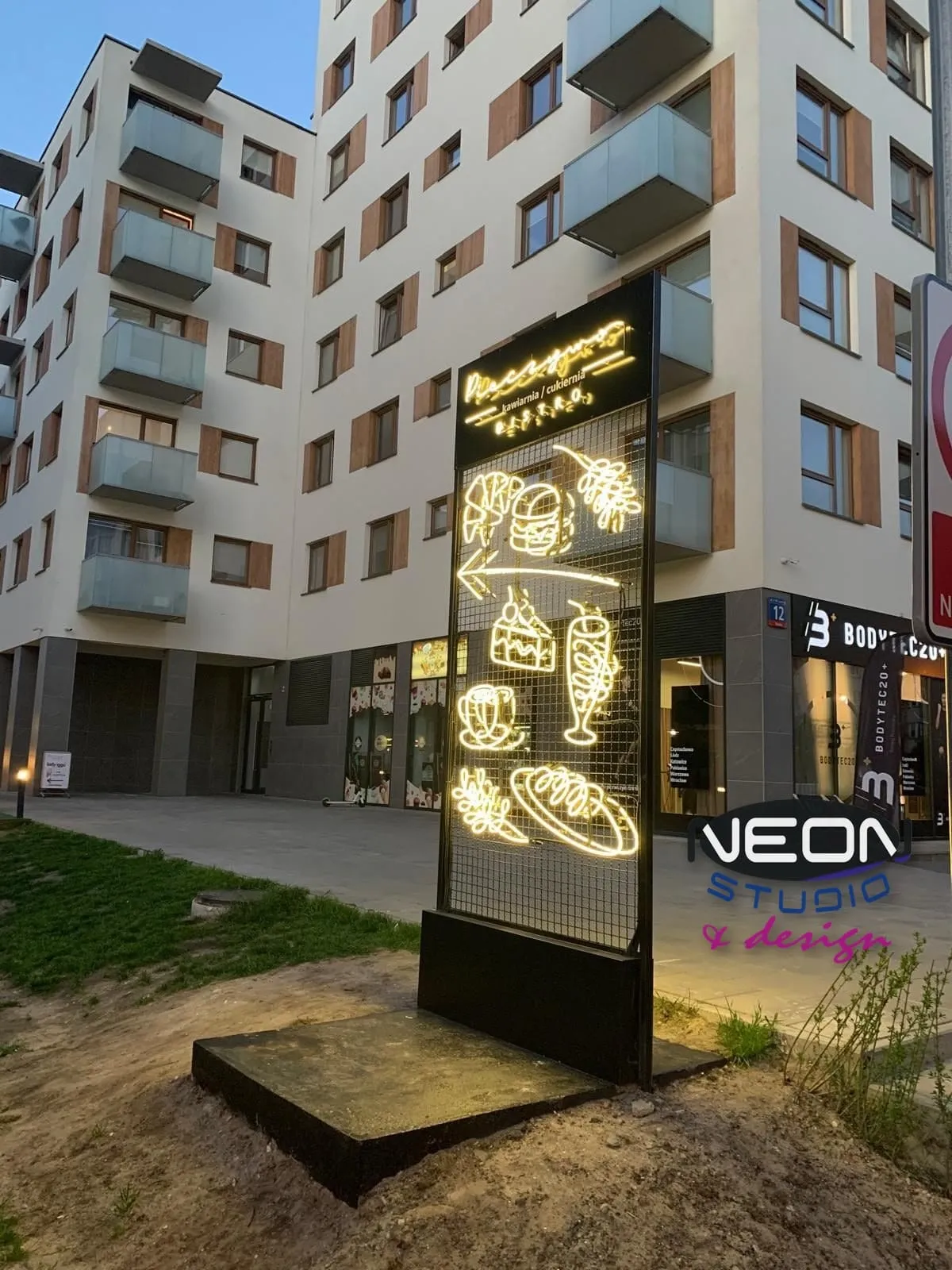 Ten sam totem z neonem szklanym od strony chodnika — kawiarnia w parterze budynku mieszkalnego